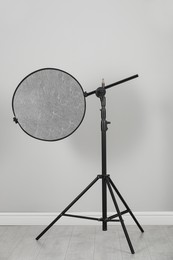 Studio reflector on tripod near grey wall indoors. Professional photographer's equipment