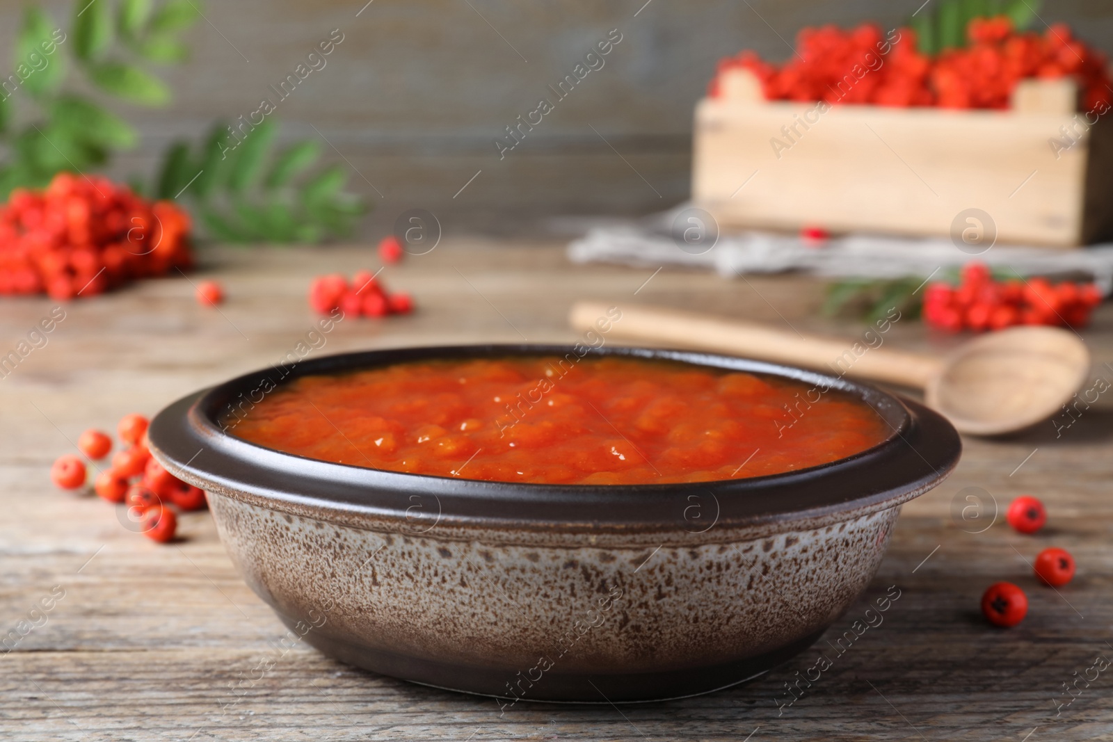 Photo of Delicious rowan jam in bowl on wooden table, closeup