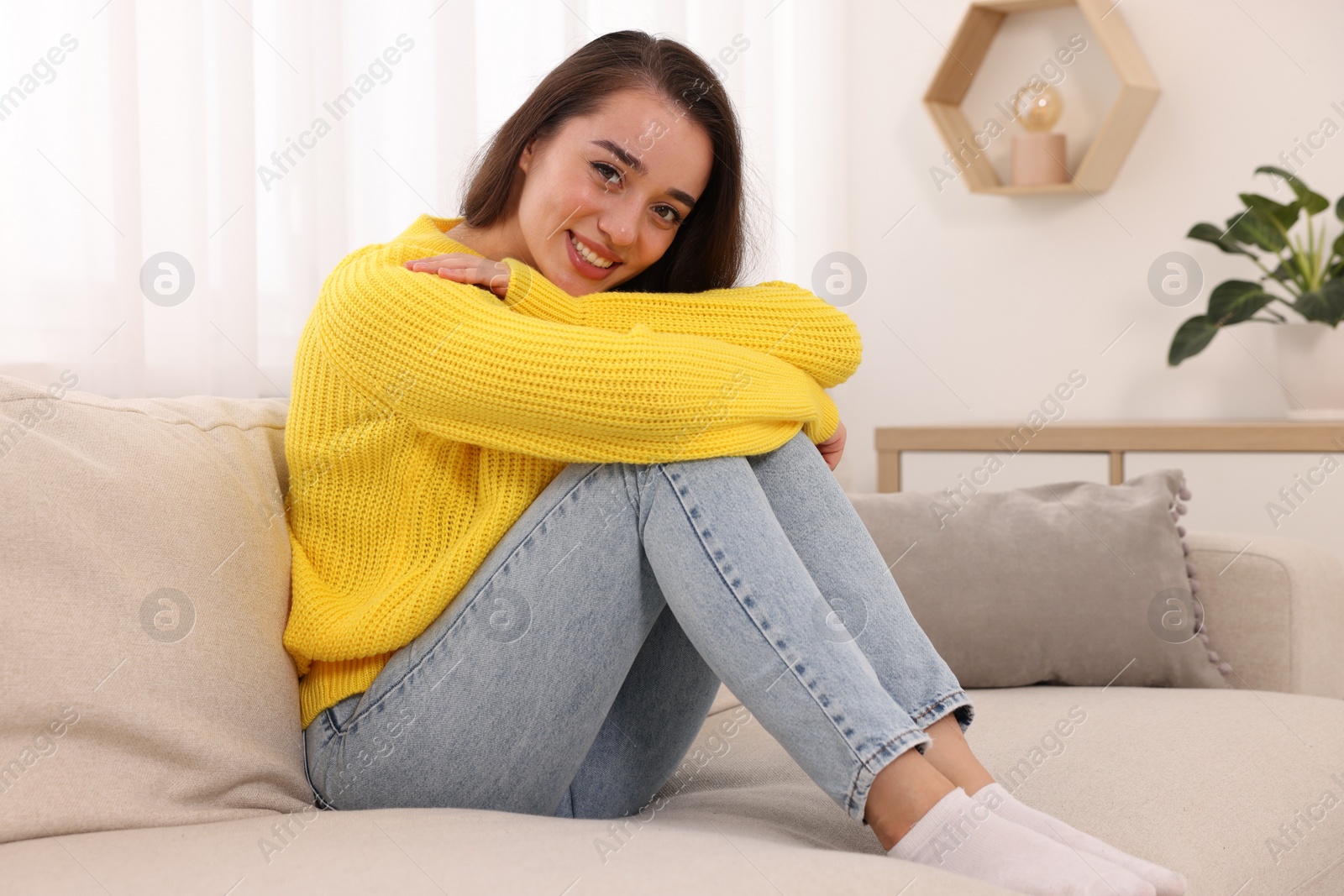 Photo of Beautiful young woman in stylish warm sweater on sofa at home