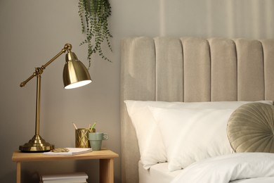Stylish golden lamp and stationery on wooden nightstand in bedroom. Interior element