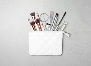 Photo of Cosmetic bag with makeup products and beauty accessories on light grey background, flat lay