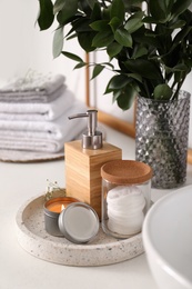 Photo of Tray with soap dispenser, cotton pads and burning candle on countertop in bathroom