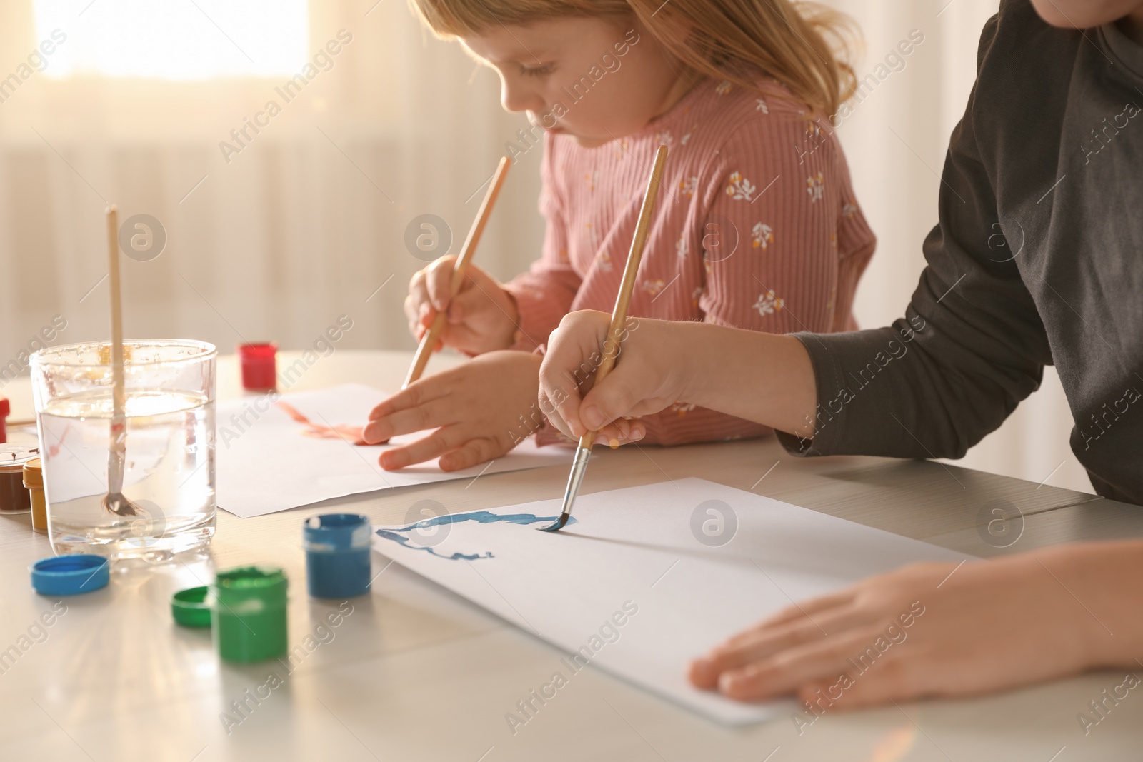 Photo of Little children drawing with brushes at wooden table indoors, closeup