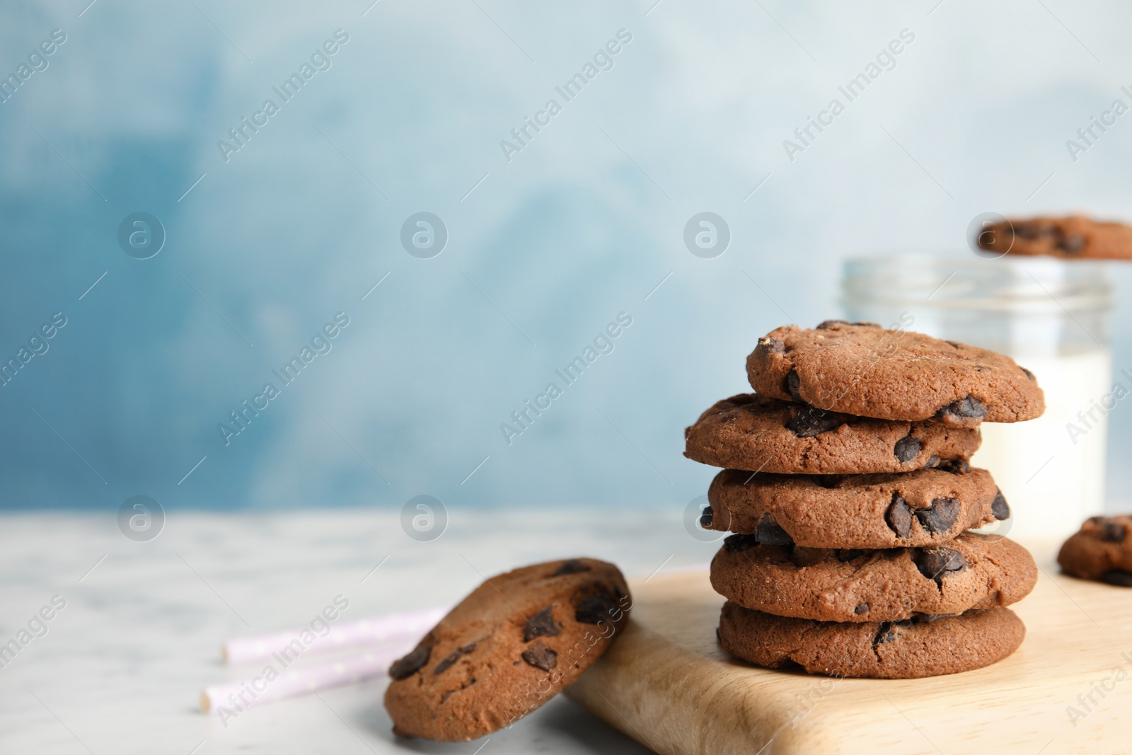 Photo of Wooden board with stack of tasty chocolate chip cookies on table. Space for text