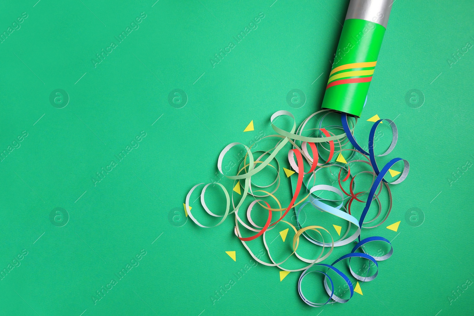 Photo of Beautiful serpentine and confetti bursting out of party popper on green background, flat lay. Space for text