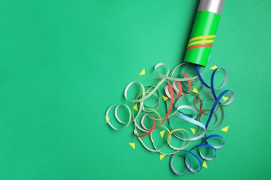 Photo of Beautiful serpentine and confetti bursting out of party popper on green background, flat lay. Space for text