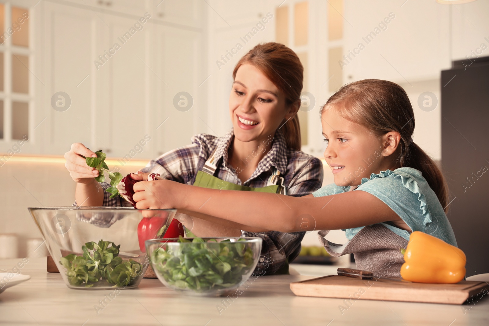 Photo of Mother and daughter cooking salad together in kitchen