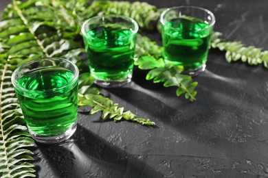 Photo of Absinthe in shot glasses and green leaves on black table, space for text. Alcoholic drink