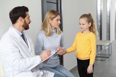 Photo of Doctor with clipboard consulting mother and daughter in clinic