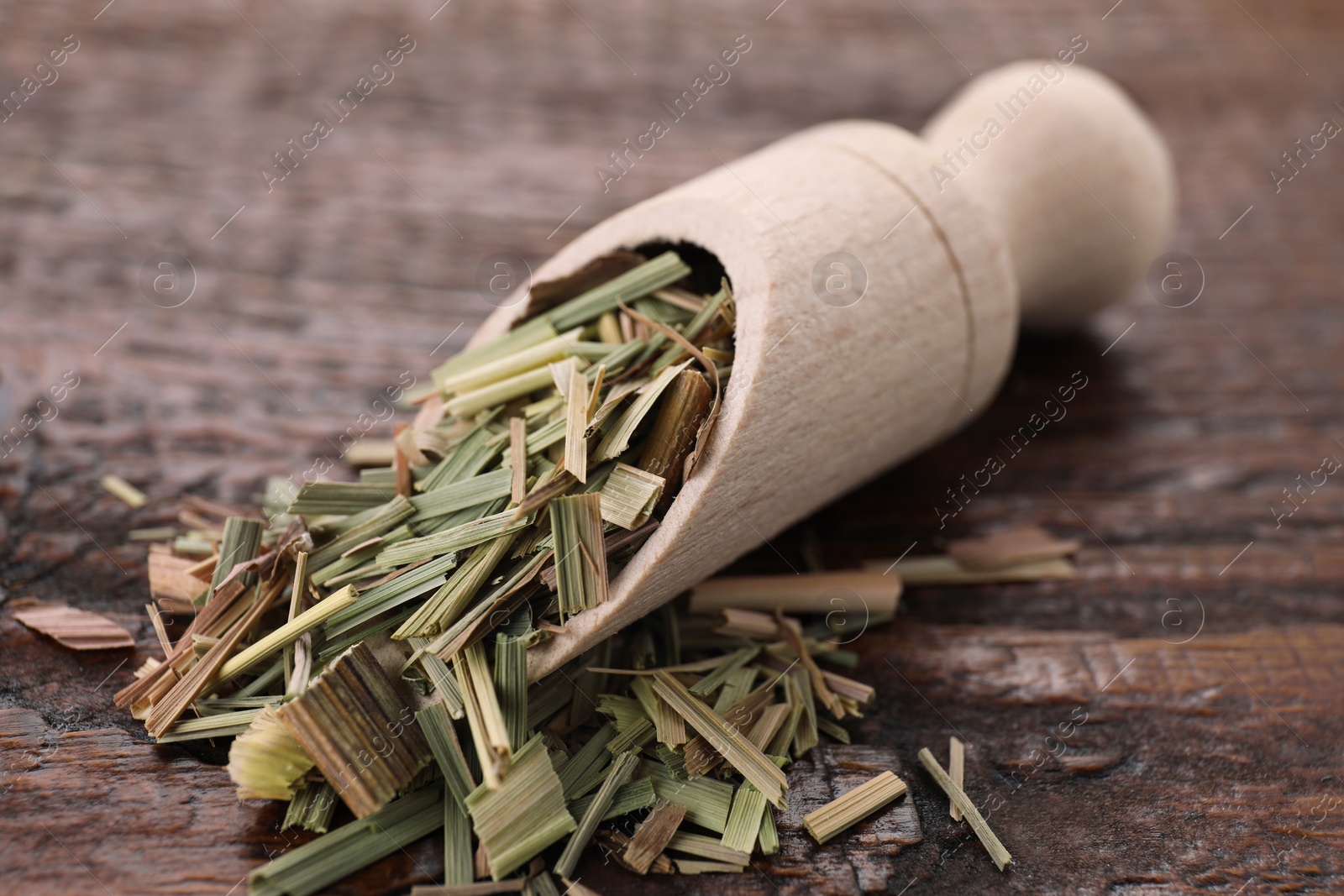 Photo of Scoop with aromatic dried lemongrass on wooden table, closeup