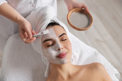 Cosmetologist applying mask on woman's face in spa salon, above view