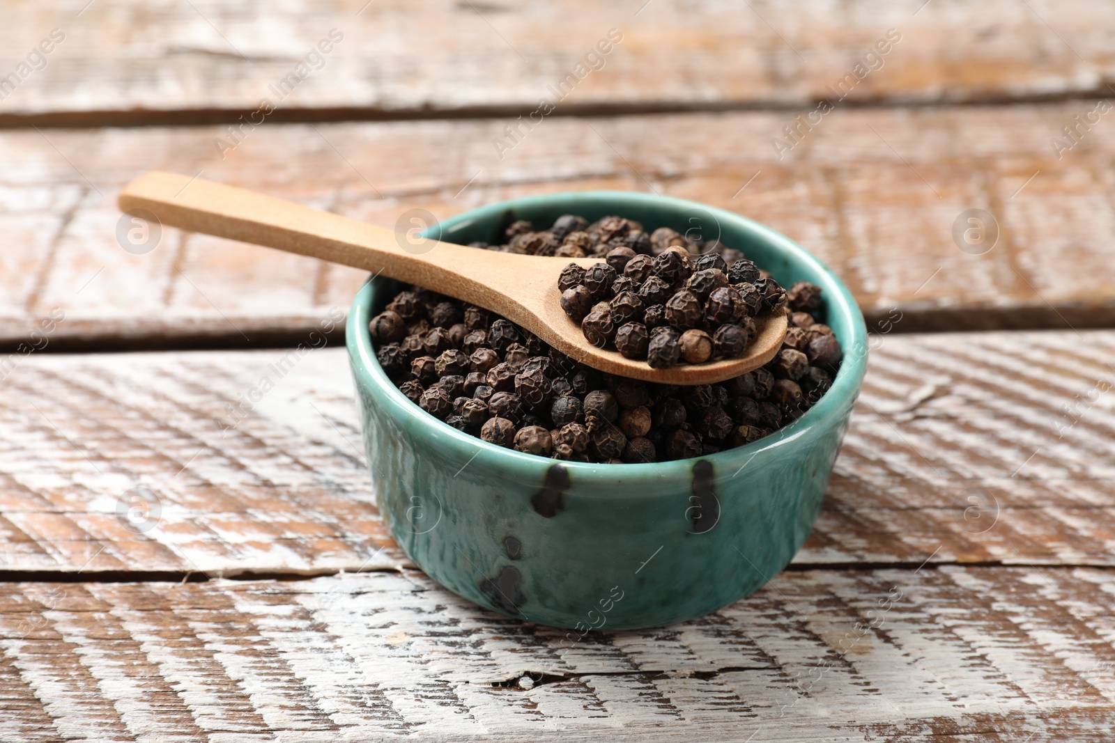 Photo of Aromatic spice. Black pepper in bowl and spoon on wooden table