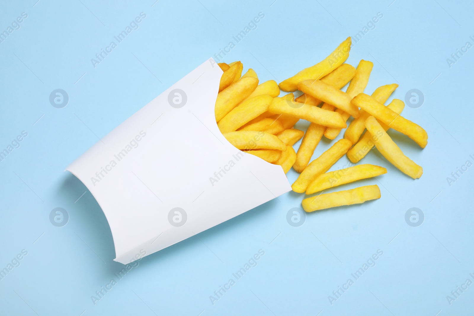 Photo of Paper cup with French fries on light blue table, above view