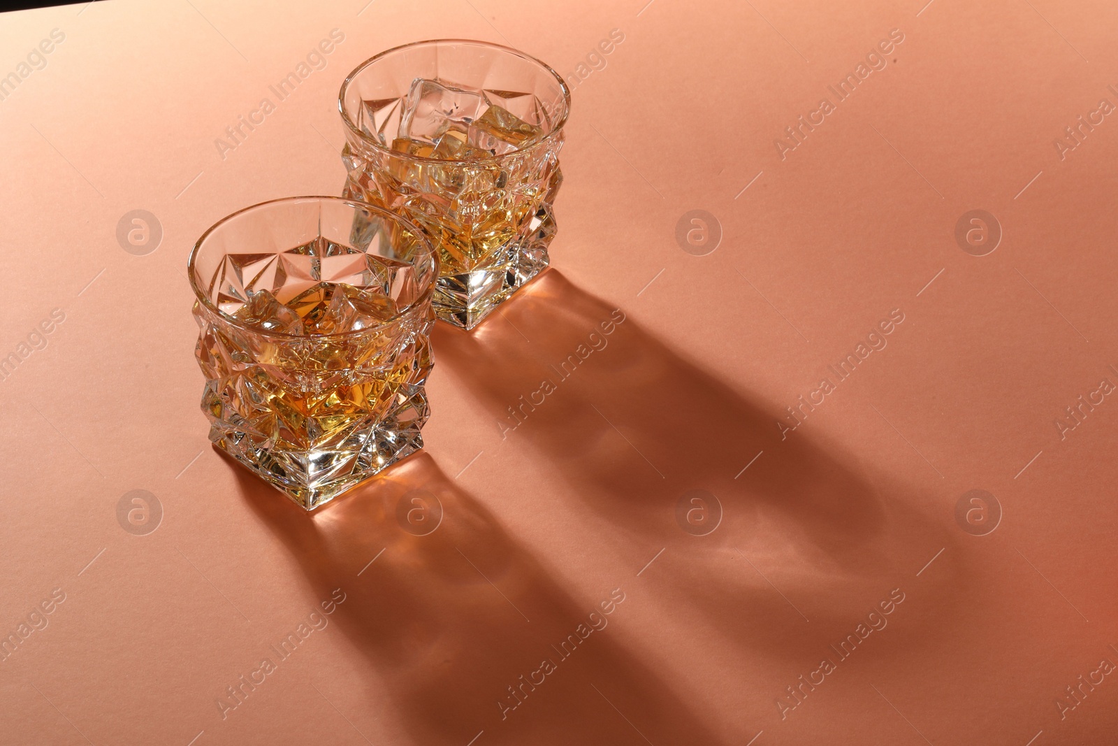 Photo of Whiskey with ice cubes in glasses on coral table, space for text