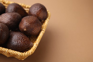 Photo of Delicious salak fruits in basket on pale brown background, closeup. Space for text