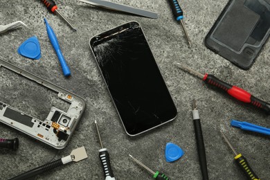 Photo of Parts of damaged smartphone and repair tool set on grey table, flat lay