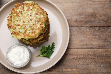 Photo of Delicious zucchini fritters with sour cream served on wooden table, top view. Space for text