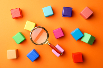 Photo of Different colorful cubes and magnifier glass on orange background, flat lay. Find keywords concept