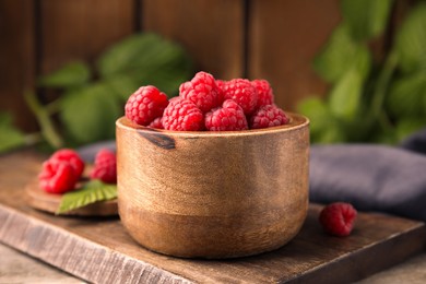 Photo of Bowl of fresh ripe raspberries on wooden board, closeup