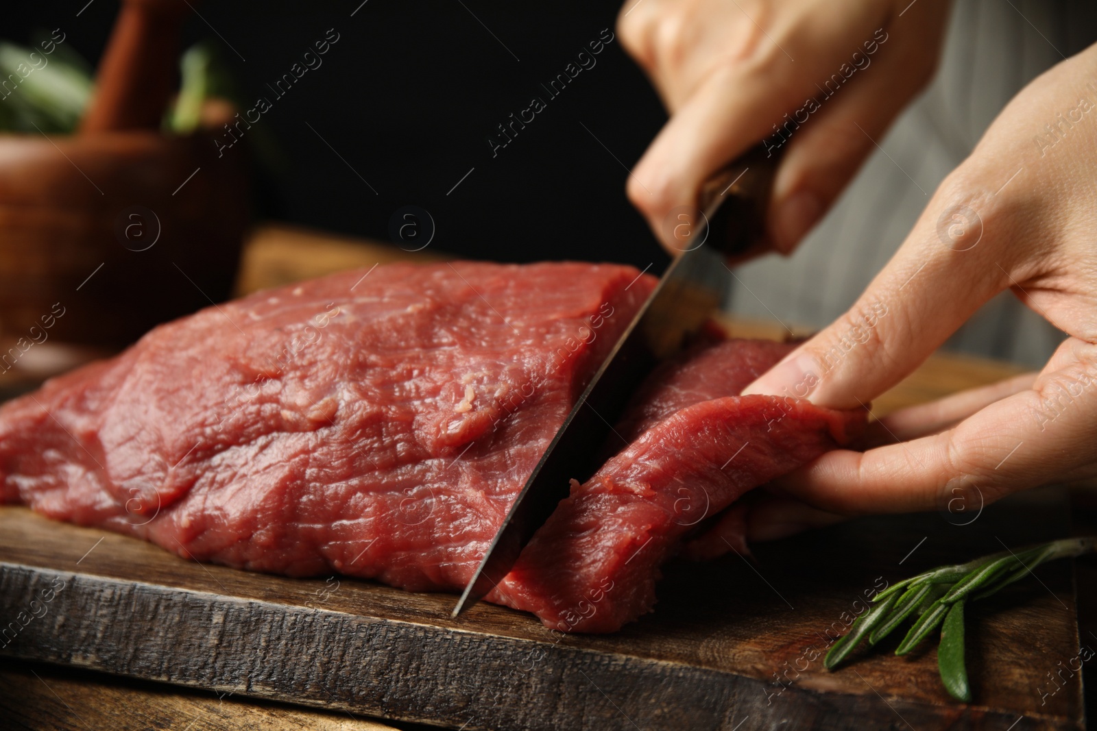 Photo of Woman cutting fresh raw meat at wooden table, closeup