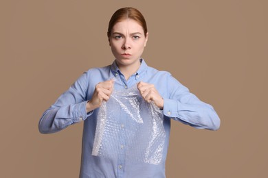 Photo of Angry woman popping bubble wrap on beige background. Stress relief