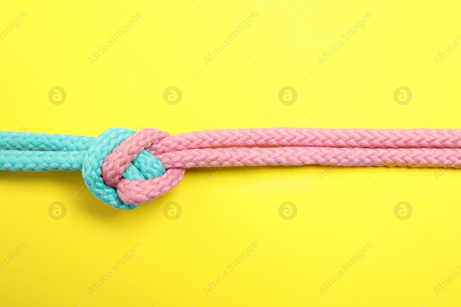 Photo of Colorful ropes tied together on yellow background, top view. Unity concept