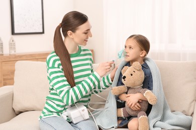 Mother helping her sick daughter with nebulizer inhalation at home