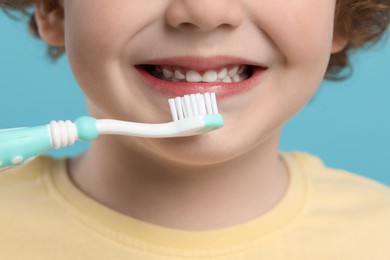 Photo of Cute little boy brushing his teeth with plastic toothbrush on light blue background, closeup