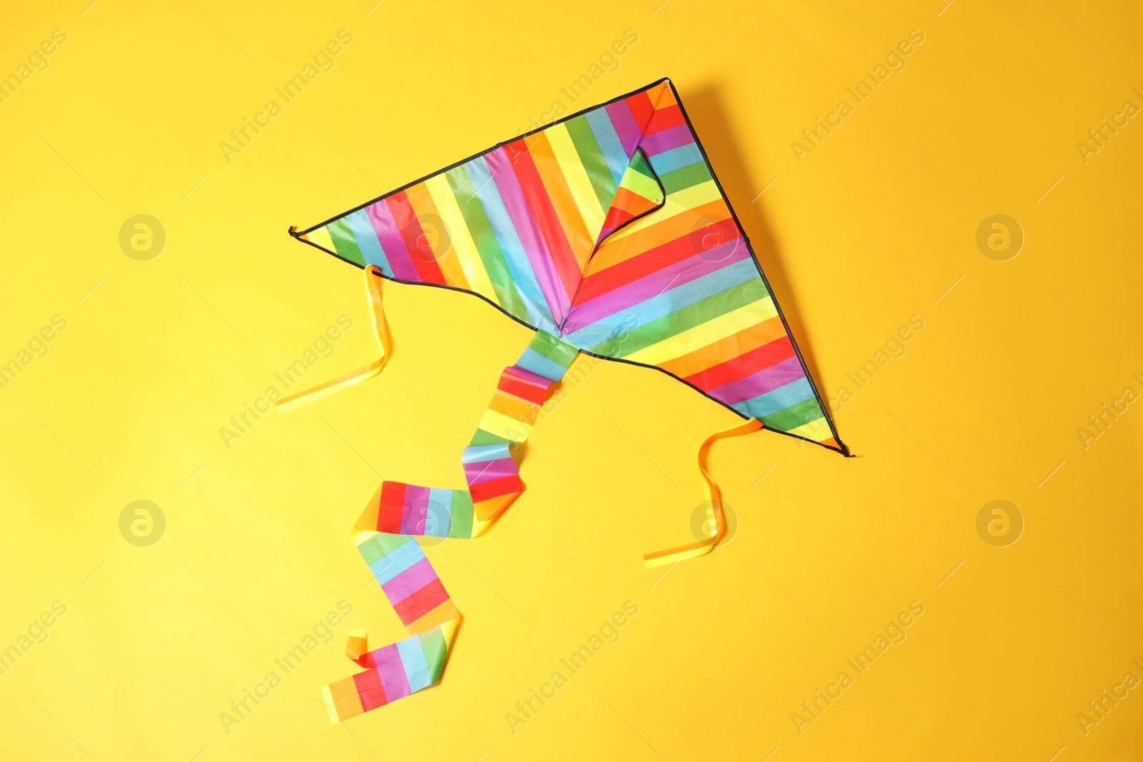 Photo of Bright rainbow kite on yellow background, top view