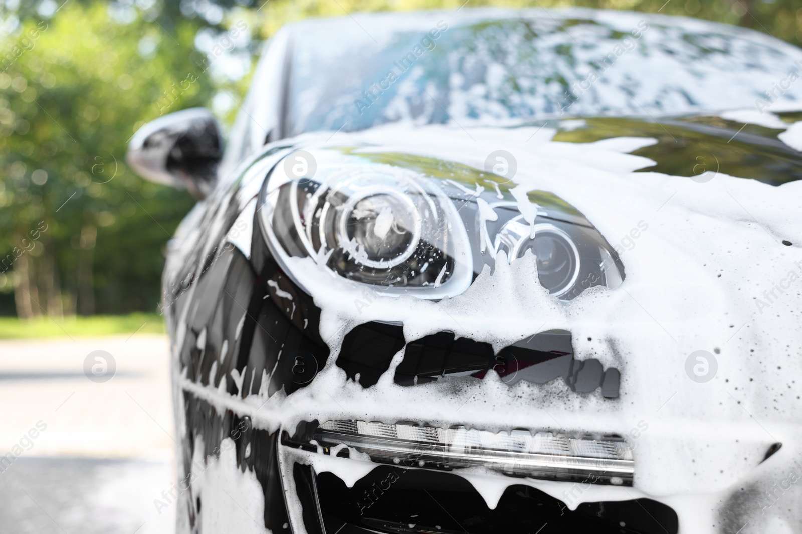 Photo of Auto covered with cleaning foam at outdoor car wash, closeup