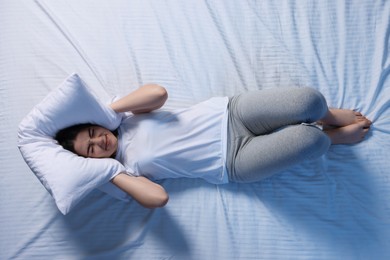 Photo of Irritated young woman covering her ears with pillow in bed, top view. Insomnia problem
