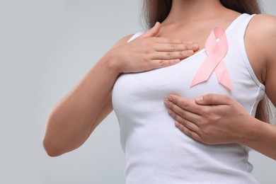 Woman with pink ribbon on light grey background, closeup. Breast cancer awareness