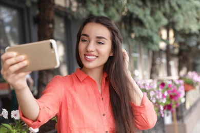 Photo of Beautiful young woman taking selfie outdoors on sunny day