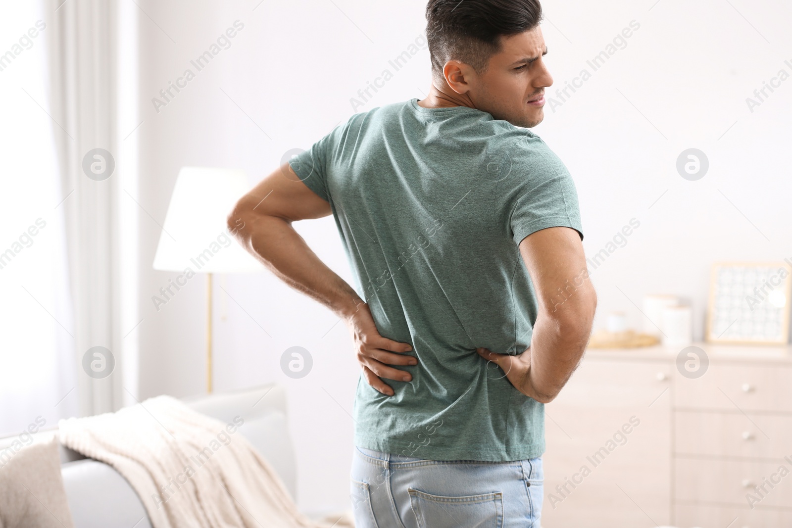 Photo of Man suffering from back pain at home. Bad posture problem