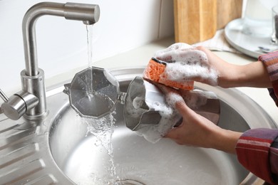 Woman washing moka pot (coffee maker) above sink in kitchen, closeup