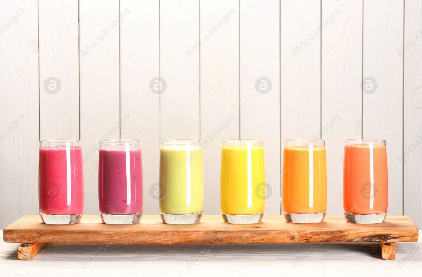 Photo of Board with many different tasty smoothies against white wooden background, space for text