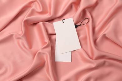 Blank white tags on pink silky fabric, top view. Space for text