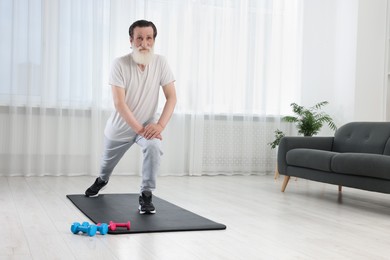 Photo of Senior man in sportswear stretching on fitness mat at home