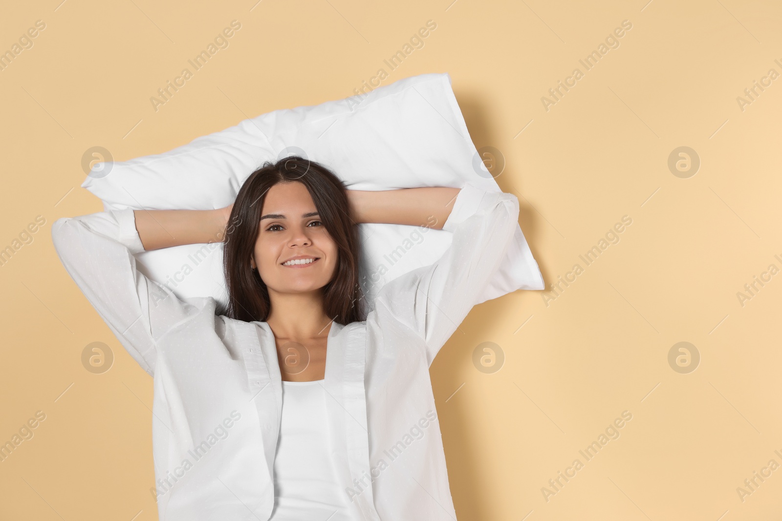 Photo of Happy young woman with soft pillow on beige background, space for text