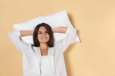 Photo of Happy young woman with soft pillow on beige background, space for text