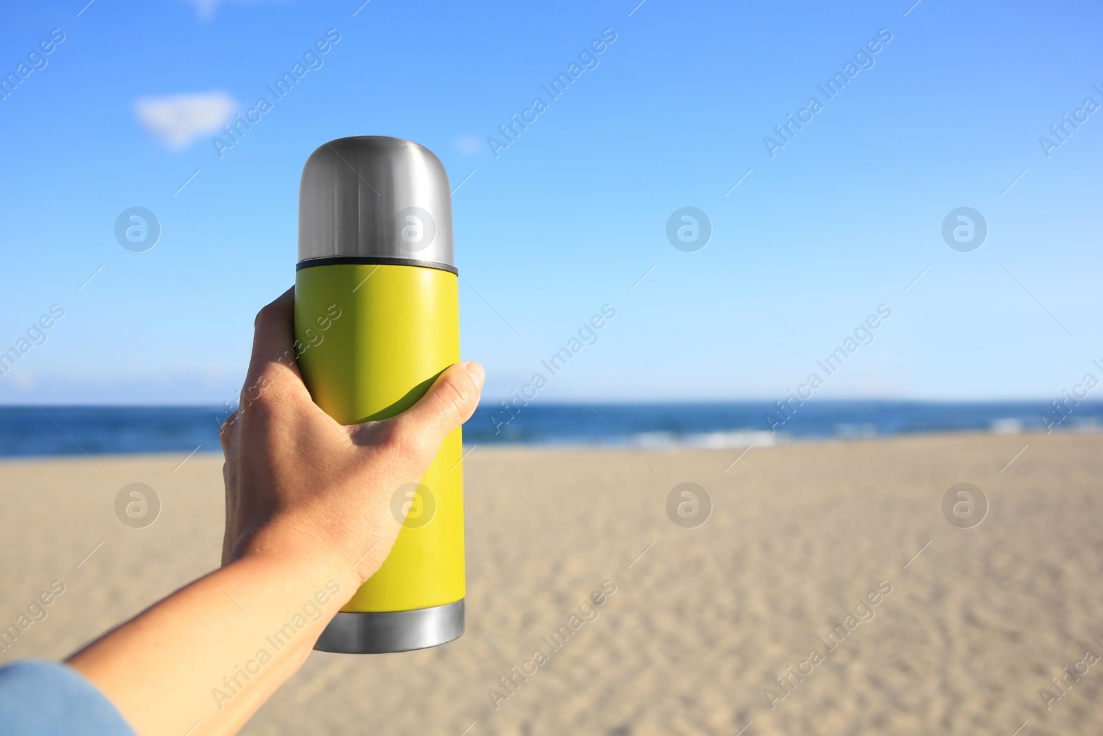 Photo of Woman holding yellow thermos with hot drink on beach near sea, closeup. Space for text