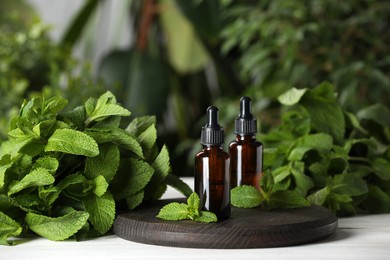 Photo of Bottles of mint essential oil and green leaves on white wooden table