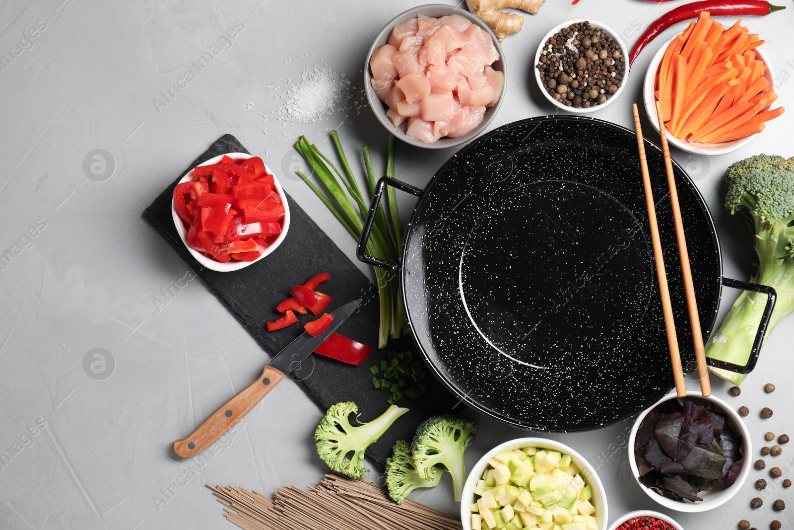 Photo of Wok pan, noodles, chicken and other products on light grey table, flat lay