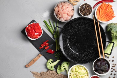 Photo of Wok pan, noodles, chicken and other products on light grey table, flat lay