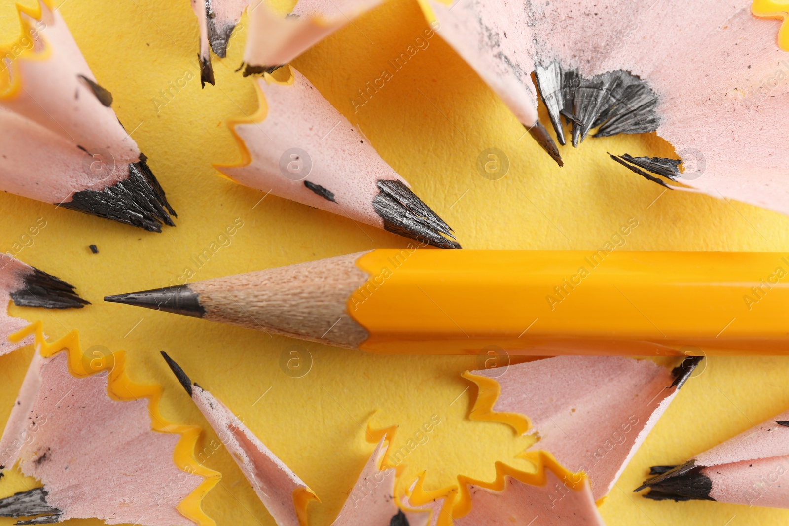 Photo of One sharp graphite pencil and shavings on yellow background, top view