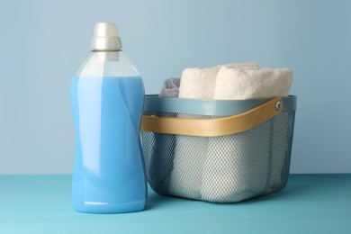 Photo of Bottle of fabric softener and towels in basket on light blue table