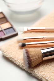 Photo of Clean makeup brushes with towel on white table, closeup