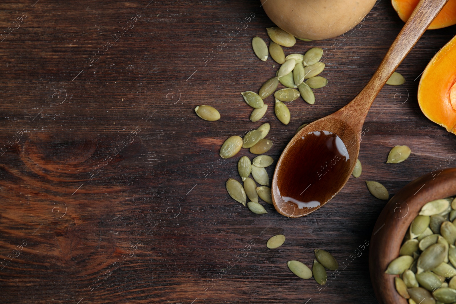 Photo of Spoon with oil and pumpkin seeds on wooden table, flat lay. Space for text