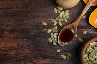 Photo of Spoon with oil and pumpkin seeds on wooden table, flat lay. Space for text