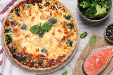 Delicious homemade quiche and ingredients on wooden table, flat lay